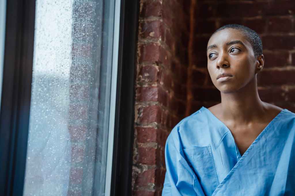 thoughtful androgynous black woman looking at window in rainy day